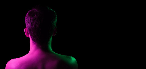 Close-up of the nape, back and shoulders of an short hair head of a man with stubble, naked without clothes, illuminated on one side in pink and on the other green on a black isolated background