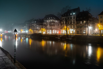 Fototapeta na wymiar Ile River Embankment in Strasbourg at night, fog. Reflections of illuminated buildings and lanterns in the water