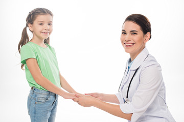 Smiling pediatrician and kid holding hands and smiling at camera isolated on white