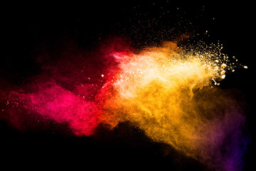 Red yellow powder explosion cloud on black background. Freeze motion of red yellow color dust  particles splashing.
