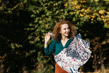 Portrait of beautiful woman with curly hair in brown skirt and green shirt running in nature. She is happy and carefree. 