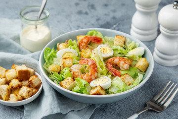 Caesar salad with prawn, roasted chicken,  croutons and cheese in blue bowl