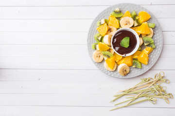 Chocolate fondue with fruit on white table. concept summer party. Copy space