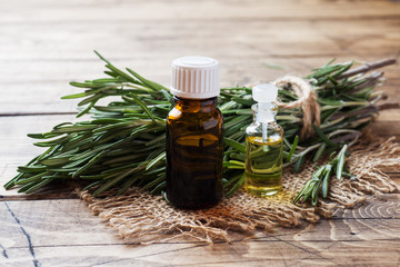 Rosemary essential oil in a glass bottle with fresh branch rosemary herb on wooden table for spa,aromatherapy and bodycare.Copy space.