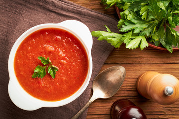 Tomato soup in a white bowl with seasonings on a wooden background