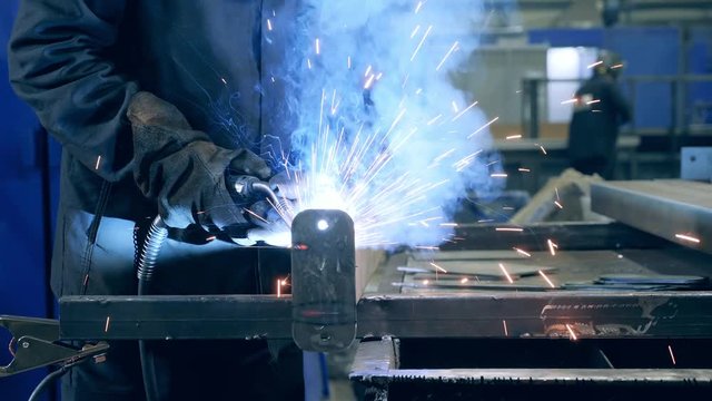 Piece of metal is getting welded by a professional. Professional Welder Working at factory facility.