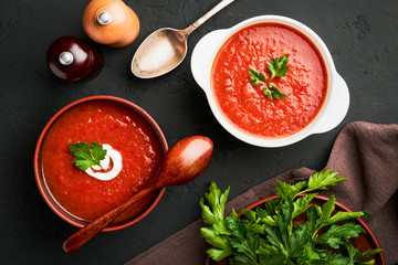 Top view of two bowls of tomato soup with parsley on a dark background