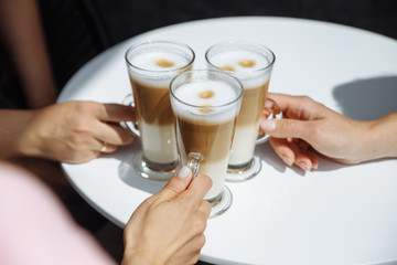 three girls holding a glass of fragrant latte coffee in their hands