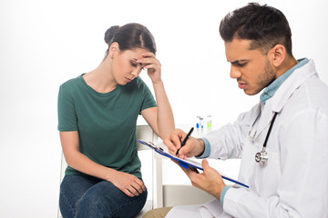 Doctor writing on clipboard near sad patient on isolated on white