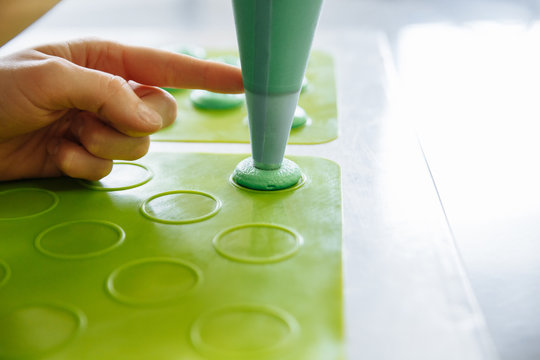 Making pink macarons. Piping out pink macaron mixture on a slip mat on backing tray, professional hands of chef making macarons with piping bag. indoor shot - Horizontal Image