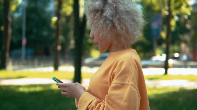 side view blonde woman scrolling touch screen on smart phone walks on the street slow motion