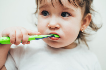 Little girl brushes her teeth with a toothbrush on a light background