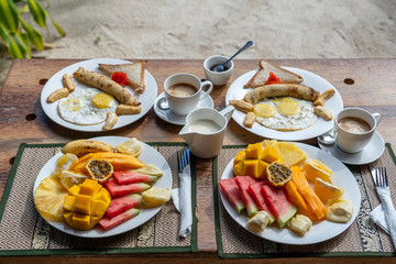 Tropical breakfast of fruit, coffee and scrambled eggs and banana pancake for two on the beach near sea