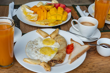 Tropical breakfast of fruit, coffee and scrambled eggs and banana pancake for two on the beach near sea