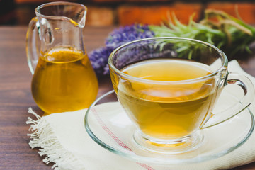 A cup of lavender tea and jar of honey with a bunch of lavender in the background