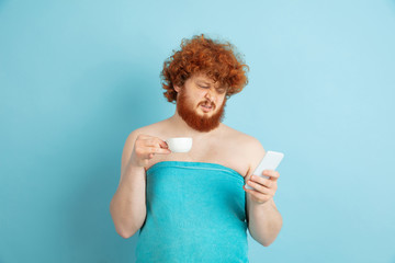 Portrait of young caucasian man in his beauty day and skin care routine. Male model with natural red hair drinking coffee and watching social media. Body and face care, natural, male beauty concept.