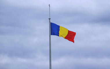 The national flag of Romania has been hoisted. In the background is a cloudy sky