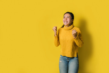 Portrait of a happy Asian woman screaming an excited and celebrating success isolated over yellow...