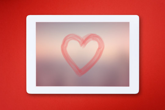 Modern digital tablet with heart shape isolated on red background