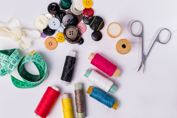 Set of spools of thread, scissors, buttons, fabrics and pins for sewing and needlework on a white background.