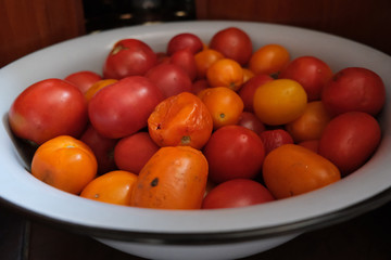Little red tomatoes in a big iron bowl on a kitchen.