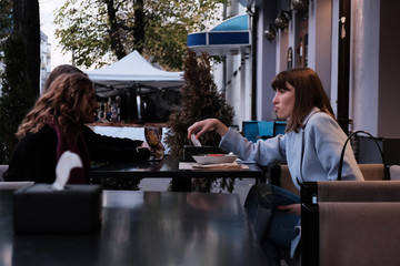 Two pretty girl friends talk and drink tea in cafe, outdoors