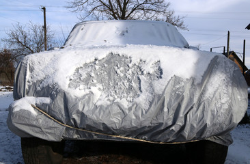 A car with a a protective cover. Car covered by snow.
