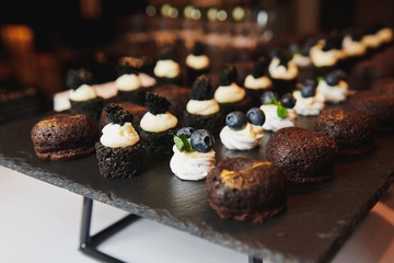 Beautiful desserts with berries and meringue at the event. Chocolate biscuit creamy. cakes Delicious sweet appetizers with cream. Stand-up meal on the black stand. Banquet catering.