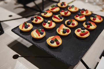 Beautiful custard baskets with berries at the event. Delicious sweet appetizers with strawberry and blueberry. Stand-up meal on the black stand. Banquet catering.