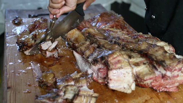 Curving and cutting a barbecued beeef or lamb ribs meat on a wooden chopping board ad putting it on a tray.