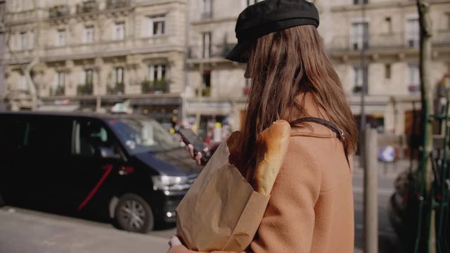 Side view beautiful elegant food blogger woman walking along Paris street with eco paper shopping bag slow motion.