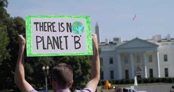 A man holds a THERE IS NO PLANET 'B' protest sign in front of the White House on a sunny summer day.  	
