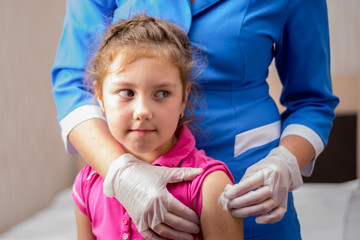 A child is vaccinated. A gloved nurse applies medical cotton to the child&rsquo;s shoulder. The little girl&rsquo;s not happy face is after vaccination. Children's medical concept