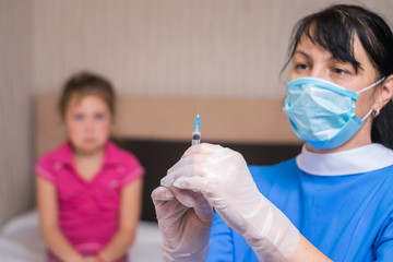 The concept of treatment and childhood vaccination. A girl in a medical mask is about to give an...