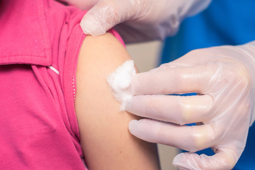 Vaccination is a close-up. A doctor in gloves presses cotton to the patient’s shoulder. Disinfection after an antiviral injection. Medical concept
