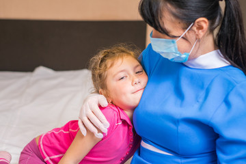 Doctor in a medical mask hugs a little girl. A nurse talking to a child about vaccination. The baby is smiling at the woman doctor. Children's medical concept. Child cuddles with a doctor