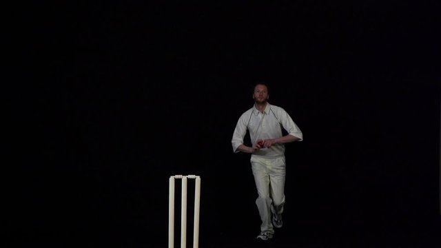 Cricket Bowler bowling the ball in a game of the sport- Black background. Dressed in White. Test Match