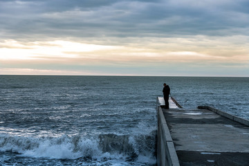 Fototapeta premium A lone traveler stands on a pier by the sea. Figure of a man on the background of the sea.