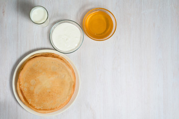 Obraz na płótnie Canvas Maslenitsa is a holiday at the end of February . pancakes with honey, sour cream and milk on a light wooden background. honey trickles down a stack of pancakes. close up. blini. space for text.