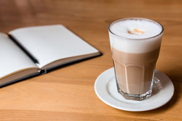 Wooden table with latte coffee and an open notebook for notes