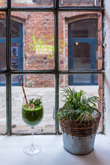An industrial window overlooking an old red brick factory. Window sill with flower and green healthy cocktail