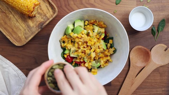 Adding pumpkin seeds to a bowl. Healthy eating concept, making healthy summer salad with vegetables. View from above.