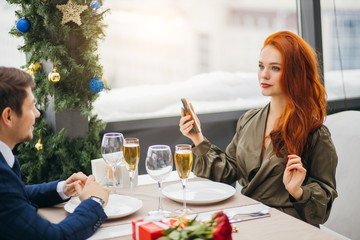 couple celebrating saint valentines day in restaurant, man and woman on a date. attractive young lady in dress and good-looking man in tuxedo sit at table drinking glass of champagne, happy together