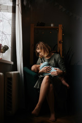 Mother and baby at home. Breastfeeding and healthy infant nutrition. Young woman nursing her newborn child sitting in white rocking chair in sunny nursery with crib and window. Parent and kid at home