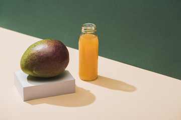 fresh juice in bottle near mango and white cube on green background