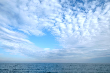 Naklejka na ściany i meble Beautiful sky landscape with white flying clouds extending over the skyline line of the sea surface