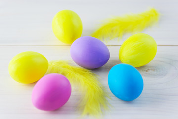 Multi-colored Easter eggs with yellow feathers on a wooden table.