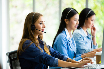 Obraz premium Attractive business woman and business man with headsets are smiling while working with computer in office