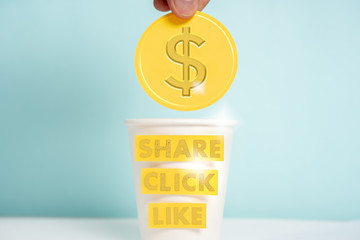 Social media, digital marketing and blog monetization concept. Golden coin with dollar symbol being thrown into a paper cup with "share", "click" and "like" labels.