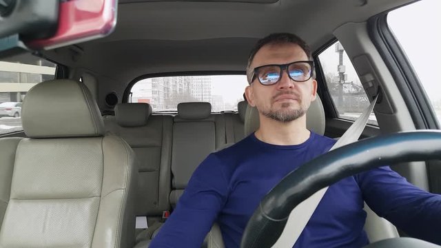 White man drives passenger car and adjusts his clothes. Strong reflection in his glasses